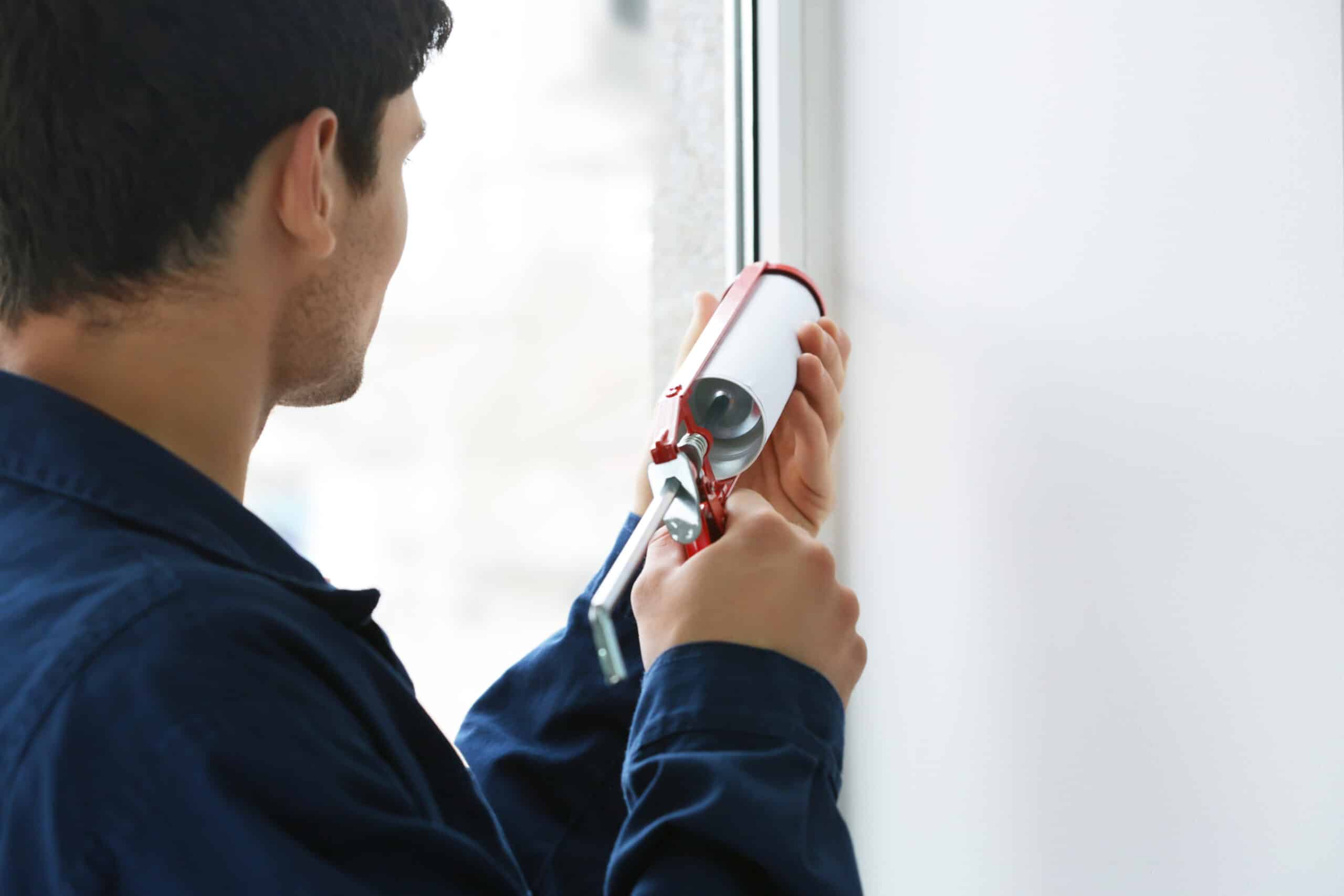 Young worker sealing joints of office window